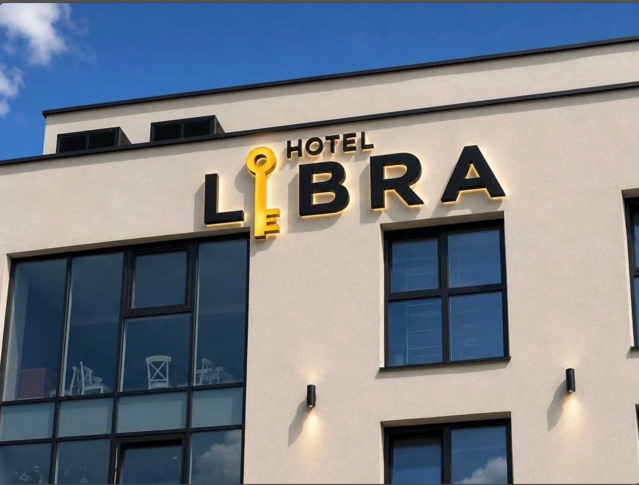 Fațada hotelului: firma HOTEL LIBRA cu cheia galbenă, pe un perete deschis, sub cer albastru